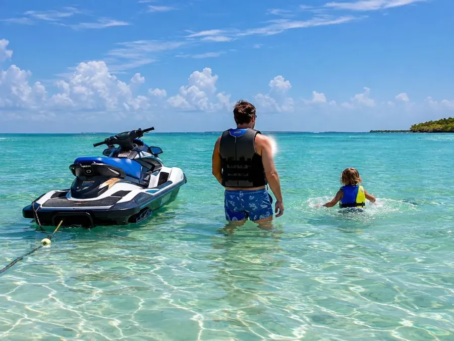 A parent and a child in life jackets standing in shallow water at a calm sandbar