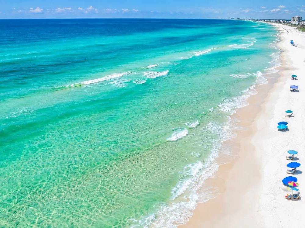 Luftaufnahme eines weißen Sandstrands und Streifen von smaragdgrünem und türkisfarbenem Wasser