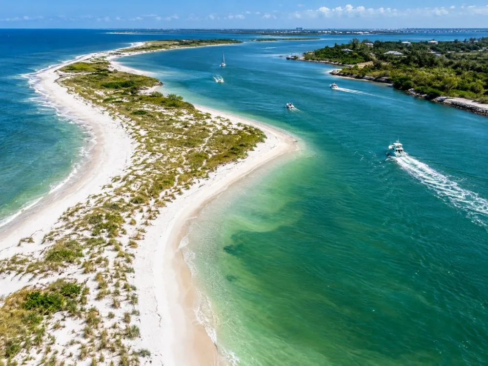 Eine weiße Sandspitze mit Strandhafer, die sich in einen grünen Gezeitenkanal krümmt